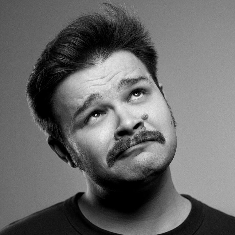 A photo of Australian voice actor, writer, and singer John Whinfield. Distinctive features include a silly expression and a very prominent mustache.